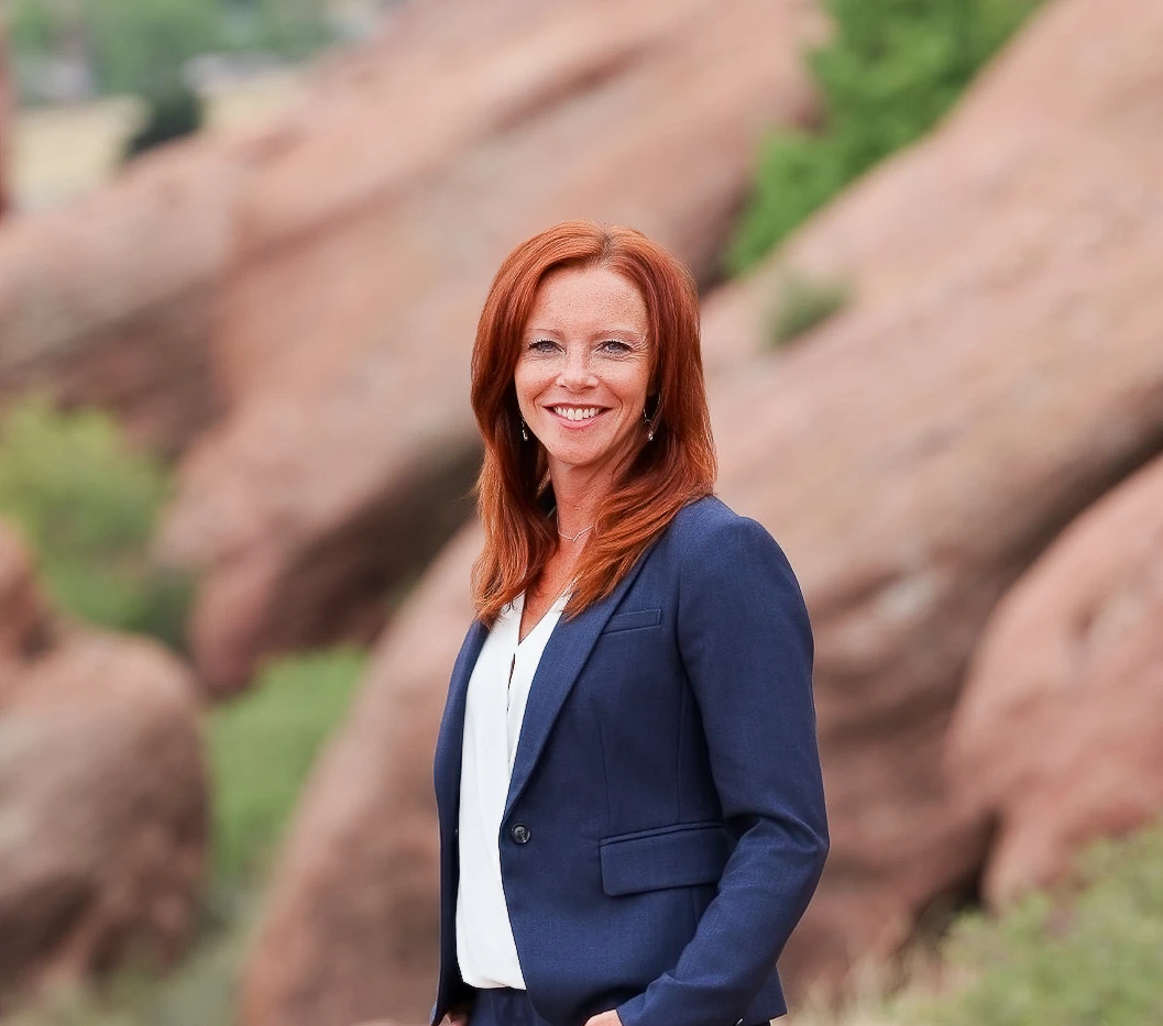 Angela Christensen smiling in a navy suit outdoors at Red Rocks